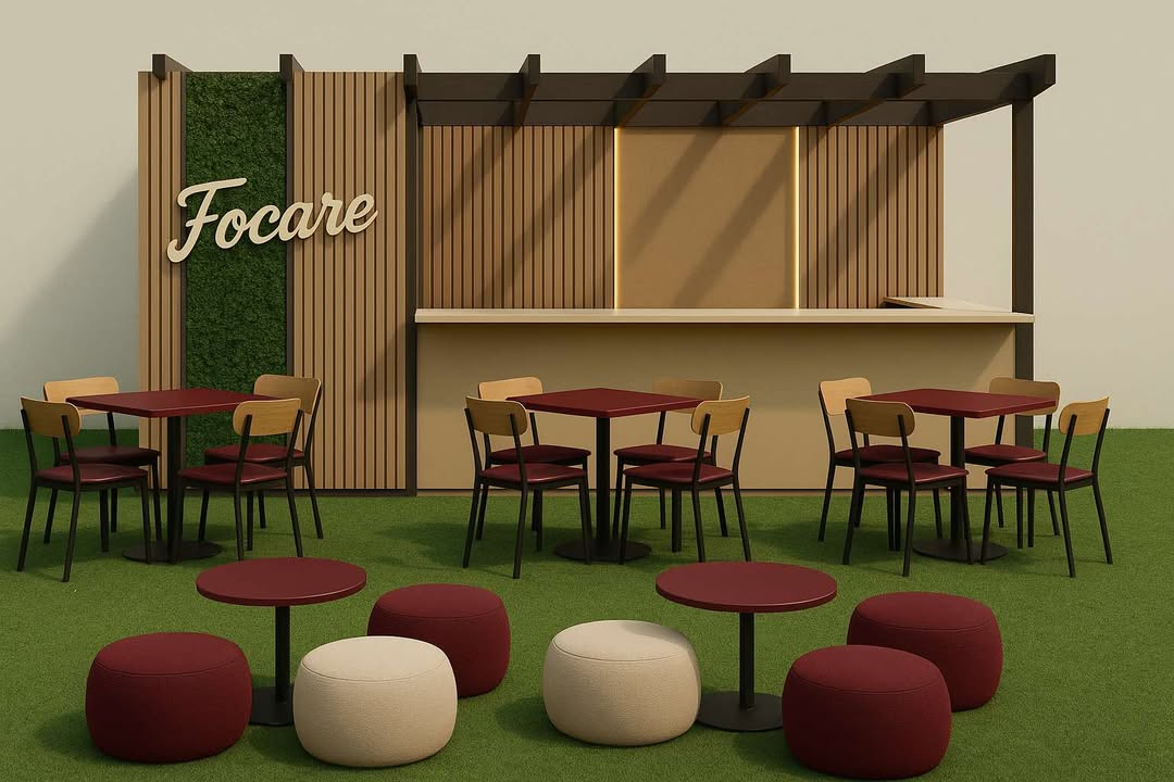 Outdoor café seating with wooden pergola, 'Focare' sign, beige bar, red tables, wooden chairs and poufs on green turf.