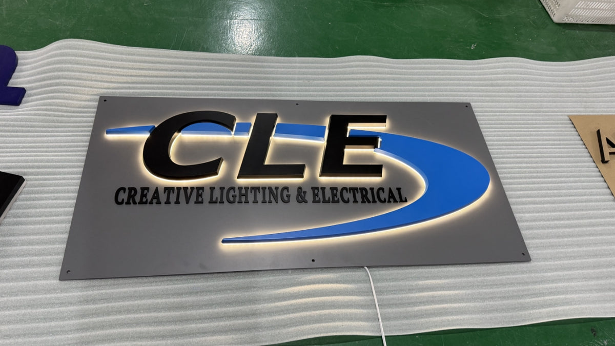 Backlit metal sign on white foam: bold black 'CLE' letters with blue swoosh and 'Creative Lighting & Electrical' text.