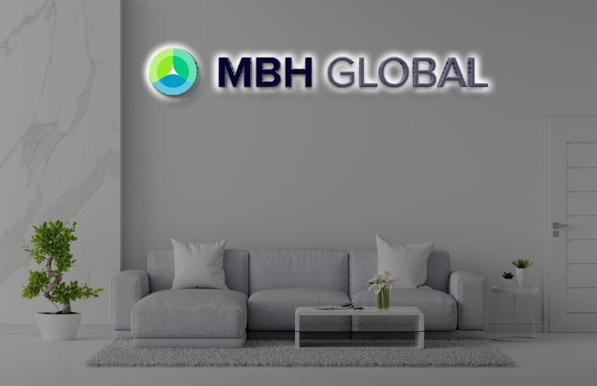 Modern gray living room with MBH Global illuminated logo above a sectional sofa, glass coffee table, potted plants.