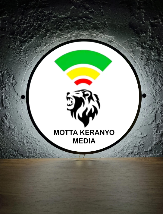 Round illuminated sign on gray textured wall: green-yellow-red Wi-Fi arcs, black roaring lion and 'MOTTA KERANYO MEDIA'.