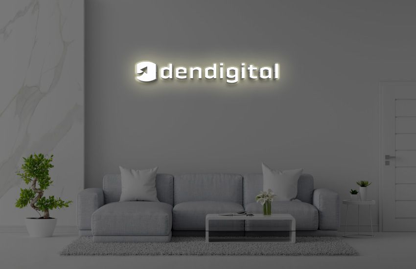 Modern gray living room with illuminated 'dendigital' logo sign above a gray sectional sofa, coffee table, potted.
