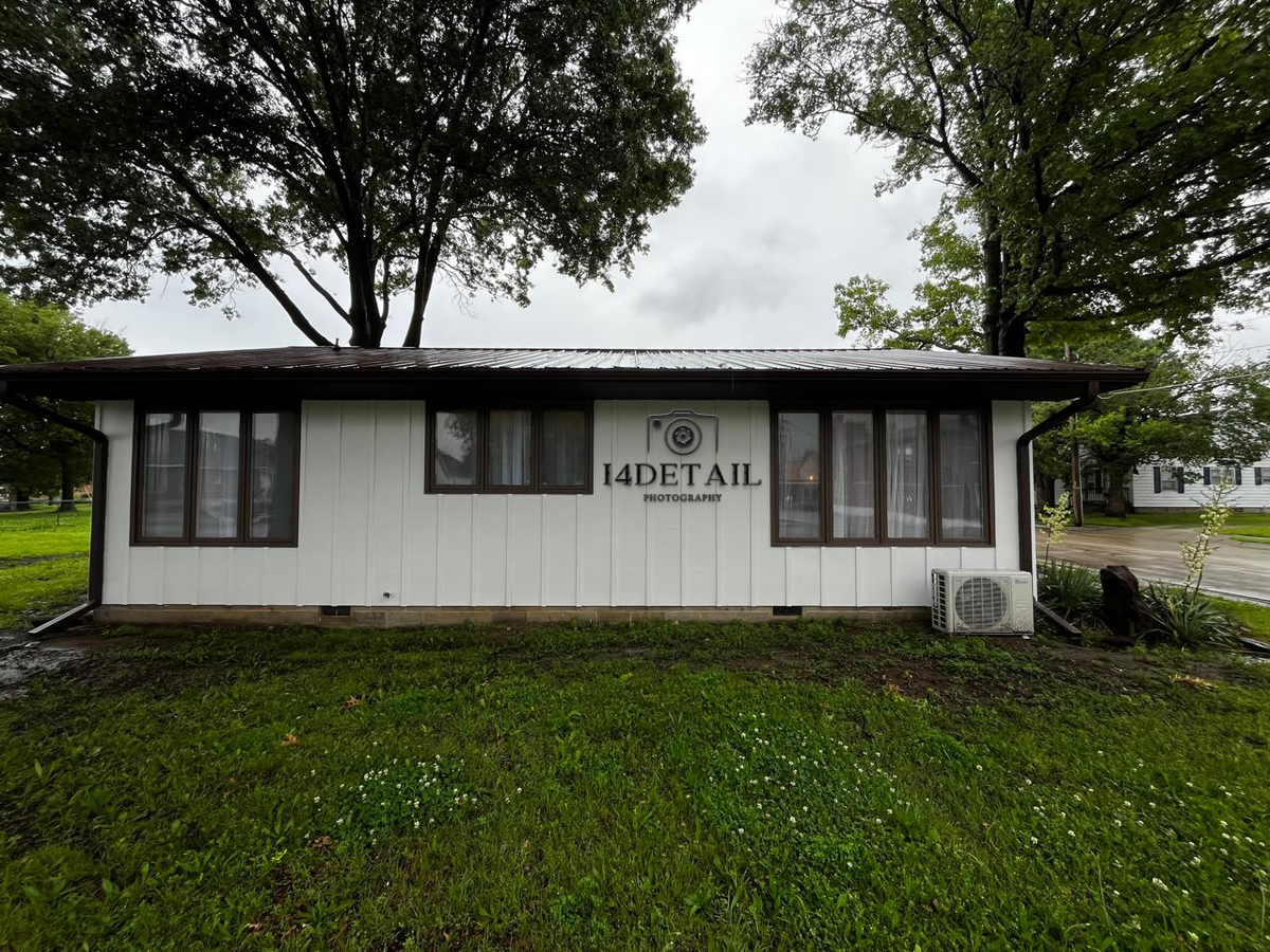 White single-story photography studio with '14DETAIL PHOTOGRAPHY' sign, brown trim windows, AC unit, grassy foreground.