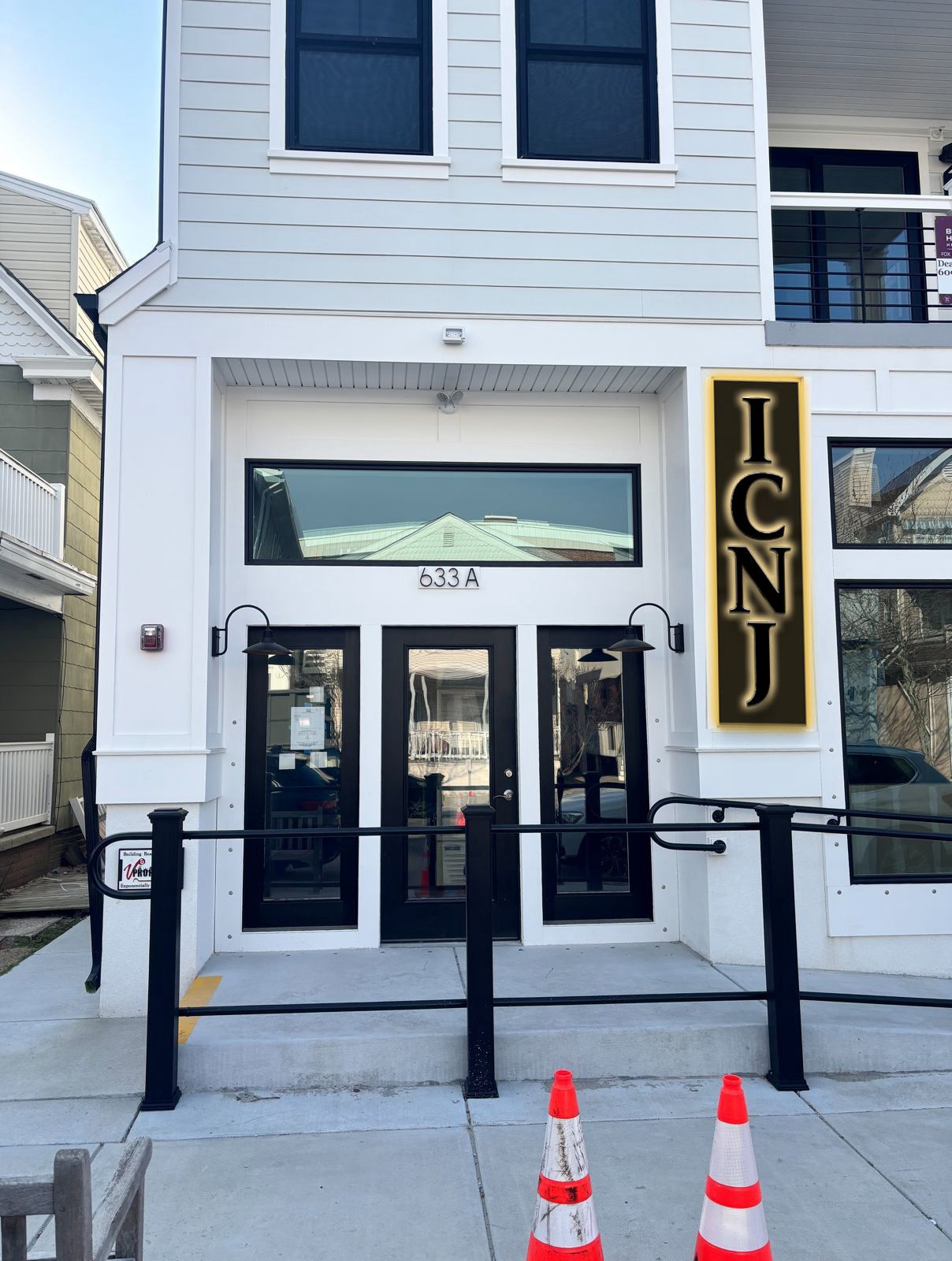 ICNJ real installed vertical storefront sign with gold lettering on black panel mounted to white facade of professional office building.