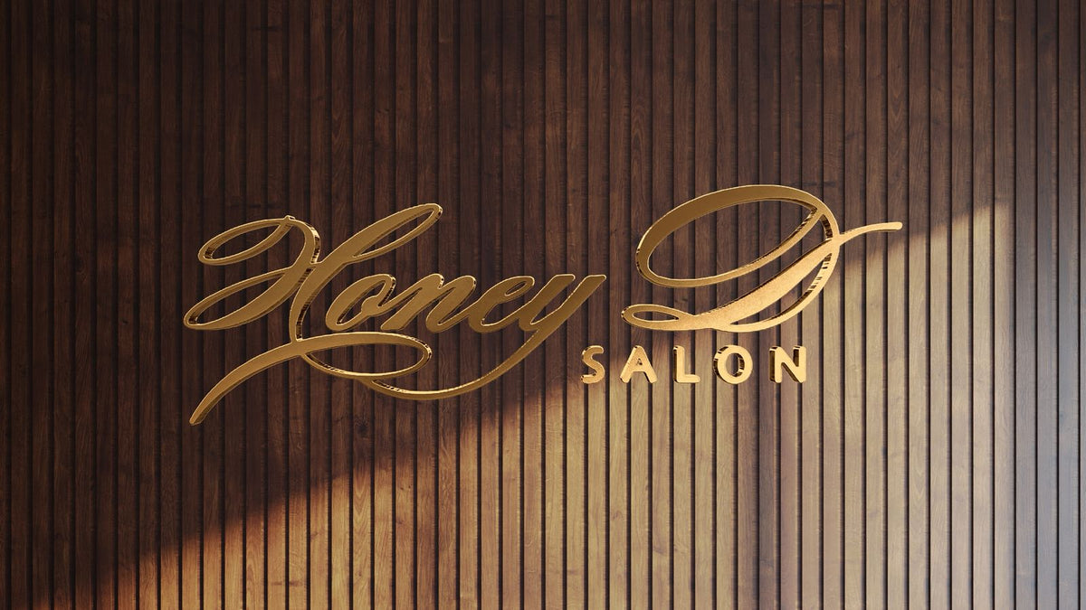 Gold metallic cursive Honey D with block SALON logo mounted on vertical dark wood slat wall with angled sunlight shadow.