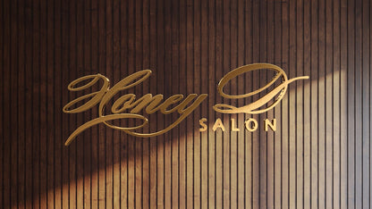 Gold metallic cursive Honey D with block SALON logo mounted on vertical dark wood slat wall with angled sunlight shadow.