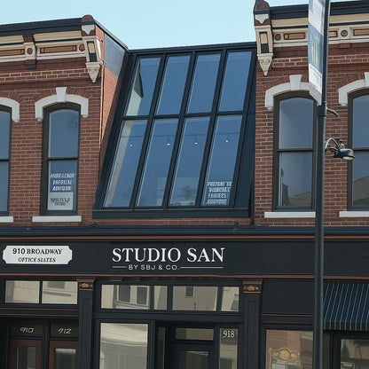 Red brick storefront on Broadway with black trim, a Studio San sign and large slanted glass windows.