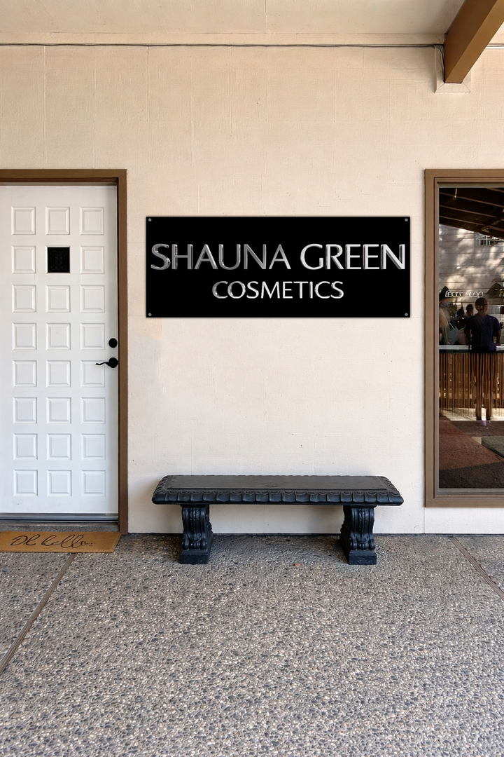 Black rectangular sign reading 'SHAUNA GREEN COSMETICS' mounted on beige wall above carved black bench.