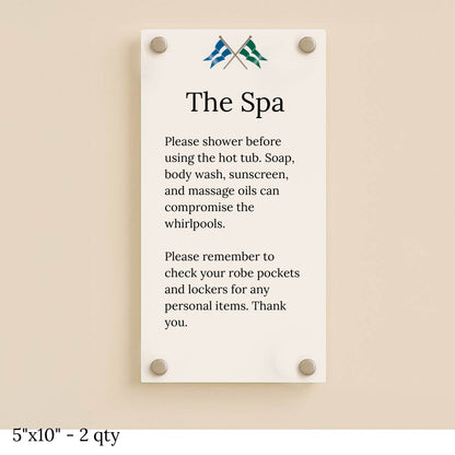 A cream glass spa sign mounted with four silver standoffs on a beige wall, titled 'The Spa' with shower rules.