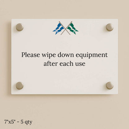 White glass sign on beige wall with four silver standoffs, crossed blue and green flags, and text to wipe equipment.