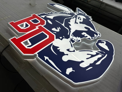 Backlit acrylic sign on workbench showing bold red 'BD' letters and navy-blue-and-white stylized mascot head.
