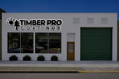 White storefront illuminated TIMBER PRO COATINGS sign with tree, windows with parked cars, entry door and green garage