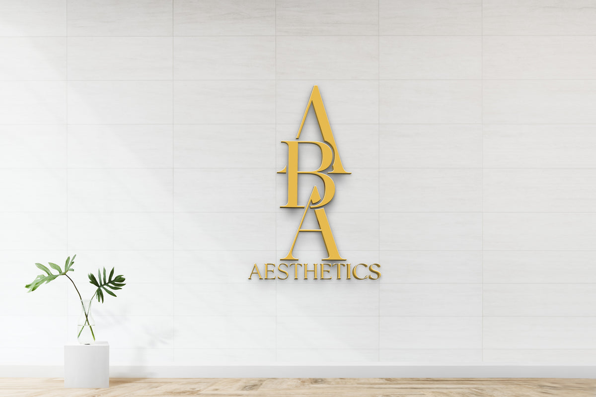 Gold vertical APA logo and gold AESTHETICS text mounted on white tiled wall, glass vase with monstera leaves on.