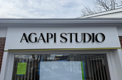 Real installed Agapi Studio storefront sign by Volt Signs, 3D polished black metal letters on white fascia, nonlit exterior business signage.