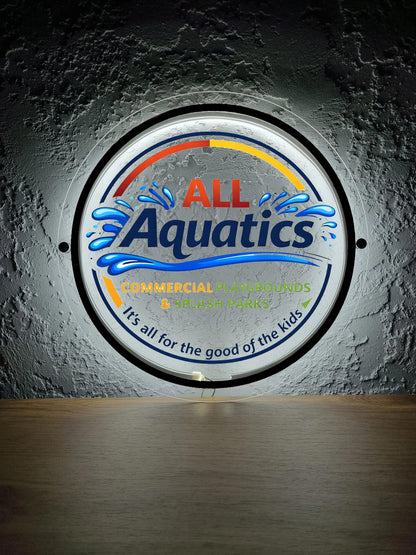 Illuminated round sign 'ALL Aquatics' with blue water splashes, orange-yellow arc, commercial playgrounds text.
