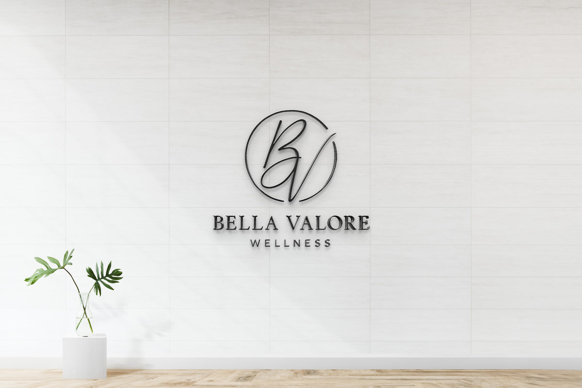 White tiled wall featuring black circular 'BV' monogram above text BELLA VALORE WELLNESS and a glass vase.
