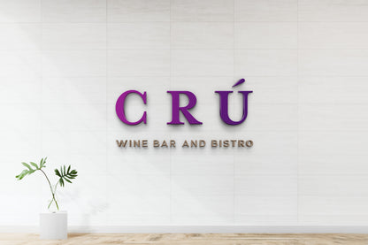 Purple 3D letters 'CRÚ' mounted on white tiled wall above gold 'WINE BAR AND BISTRO' text, vase with green leaves.