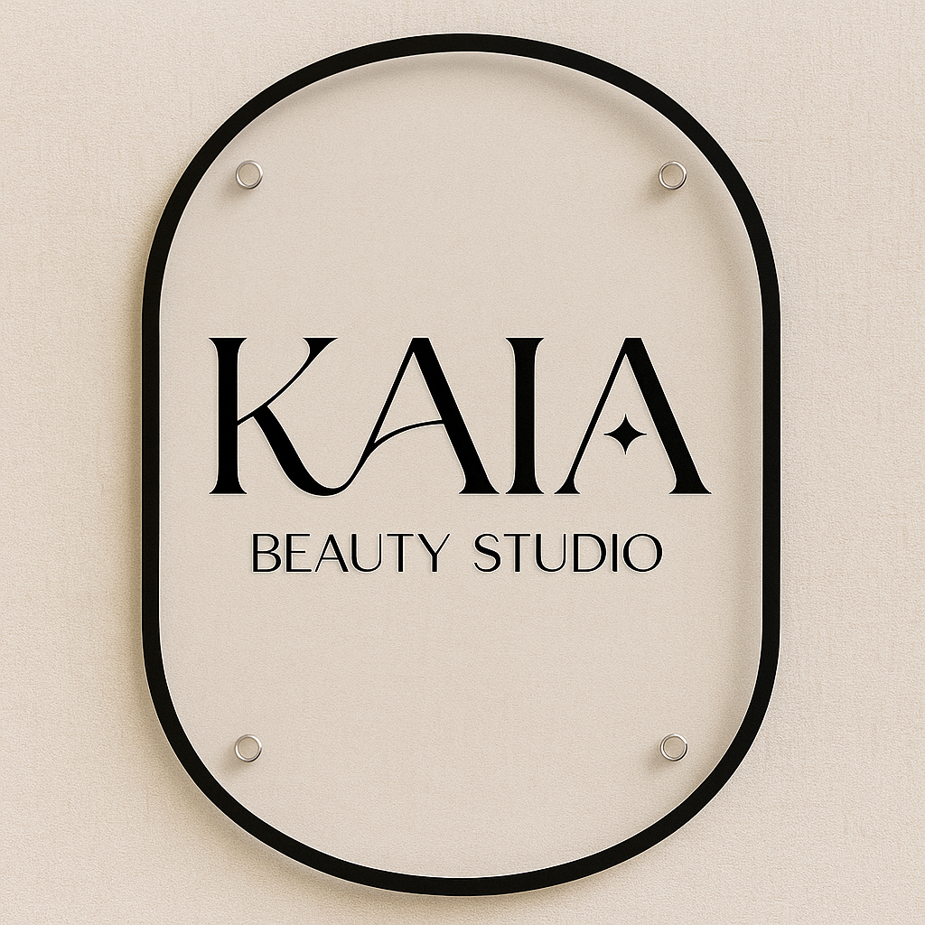 Black KAIA Beauty Studio sign with serif text on a beige background, framed by a thin black oval and silver studs.