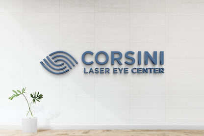 Blue 3D 'CORSINI LASER EYE CENTER' sign and circular wave logo on white tiled wall above glass vase plant.