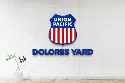 Union Pacific blue shield logo with red-white stripes above bold DOLORES YARD text on white tiled wall, vase plant left