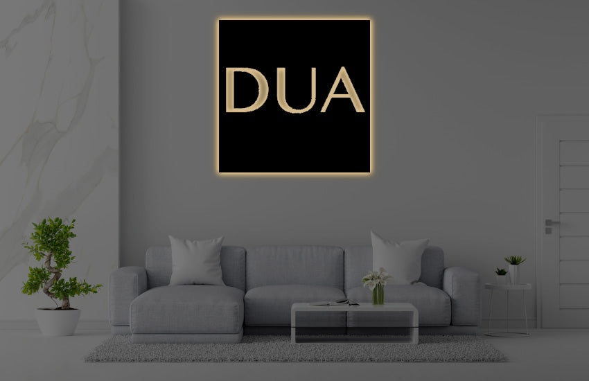 Modern living room with gray sectional sofa, coffee table, plants and black wall art 'DUA' in gold illuminated frame.
