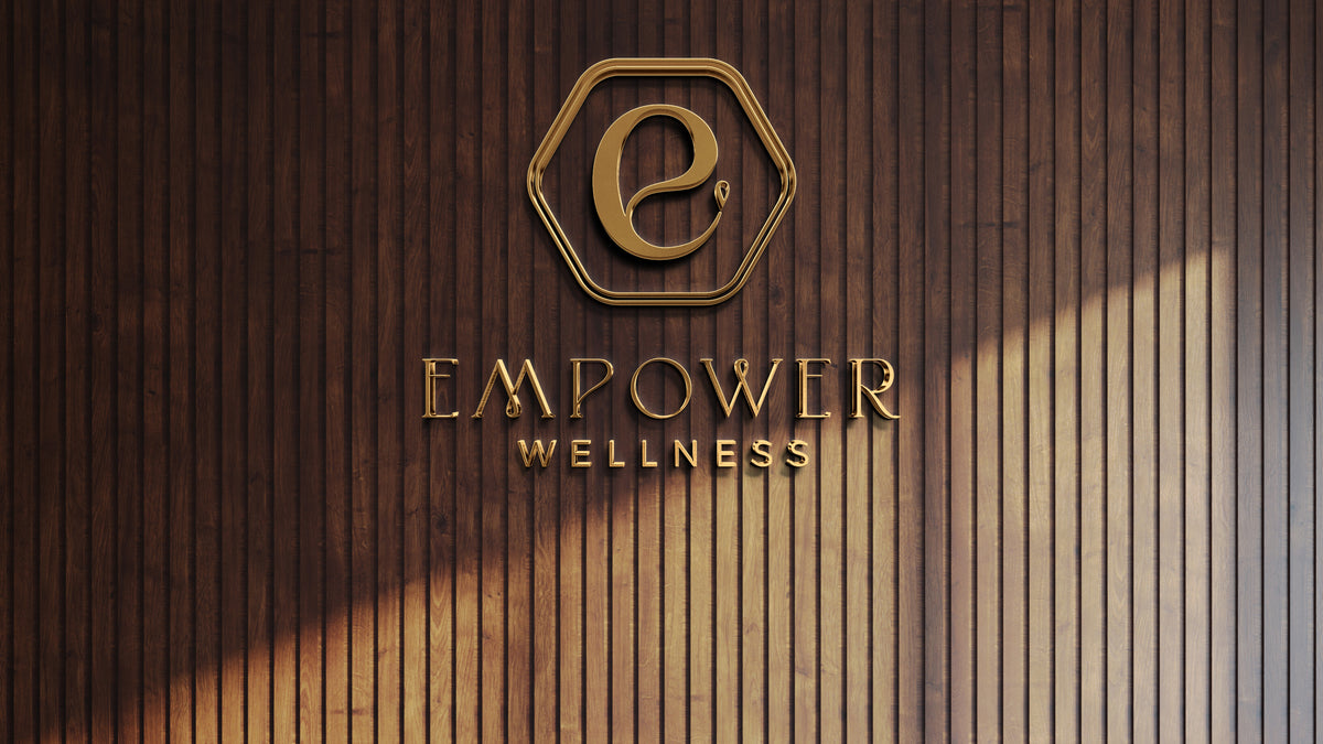 Gold hexagon emblem with stylized 'e' and metallic EMPOWER WELLNESS lettering mounted on vertical dark wood slat wall.