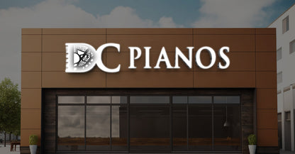 DC Pianos storefront with white illuminated logo on brown panel facade, large glass windows and potted greenery.