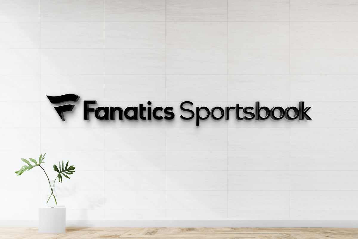 Black 3D 'Fanatics Sportsbook' sign and stylized F logo on white tiled wall above glass vase with monstera.