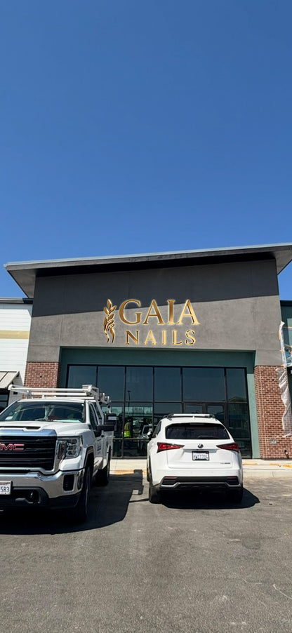 GAIA NAILS storefront with gold lettering above glass doors, white GMC truck and white Lexus SUV parked.