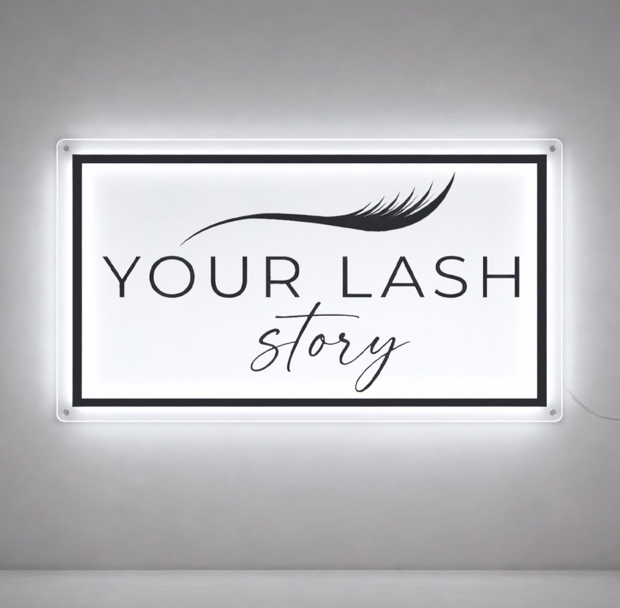 Your Lash Story rectangular halo backlit clear acrylic sign with lash illustration and script tagline, lash salon interior with bright white LED glow.
