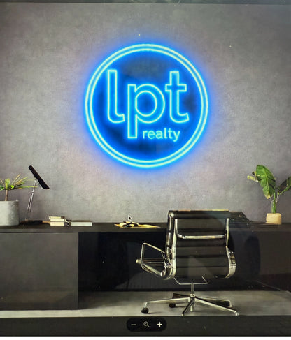 Gray office wall with glowing blue circular 'lpt realty' neon logo above black desk and swivel chair, lamp, plants.