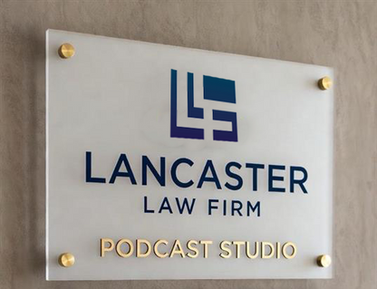 Frosted acrylic plaque 'LANCASTER LAW FIRM' in navy with blue logo and gold 'PODCAST STUDIO' on beige wall.