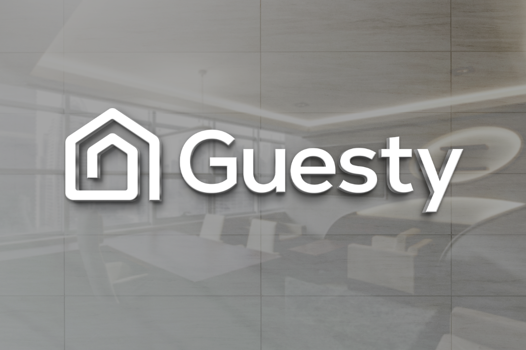 White 3D 'Guesty' logo and white house-shaped icon centered over blurred gray modern office interior with sofas.