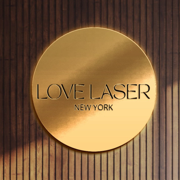 Gold circular wall plaque reading LOVE LASER NEW YORK on a wood slat background, Volt Signs custom sign and signage