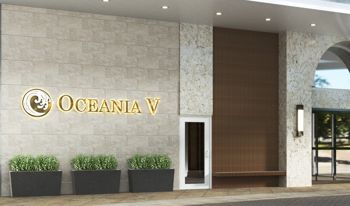Exterior building entrance with gold illuminated OCEANIA V sign and wave logo on beige stone wall, three planters.