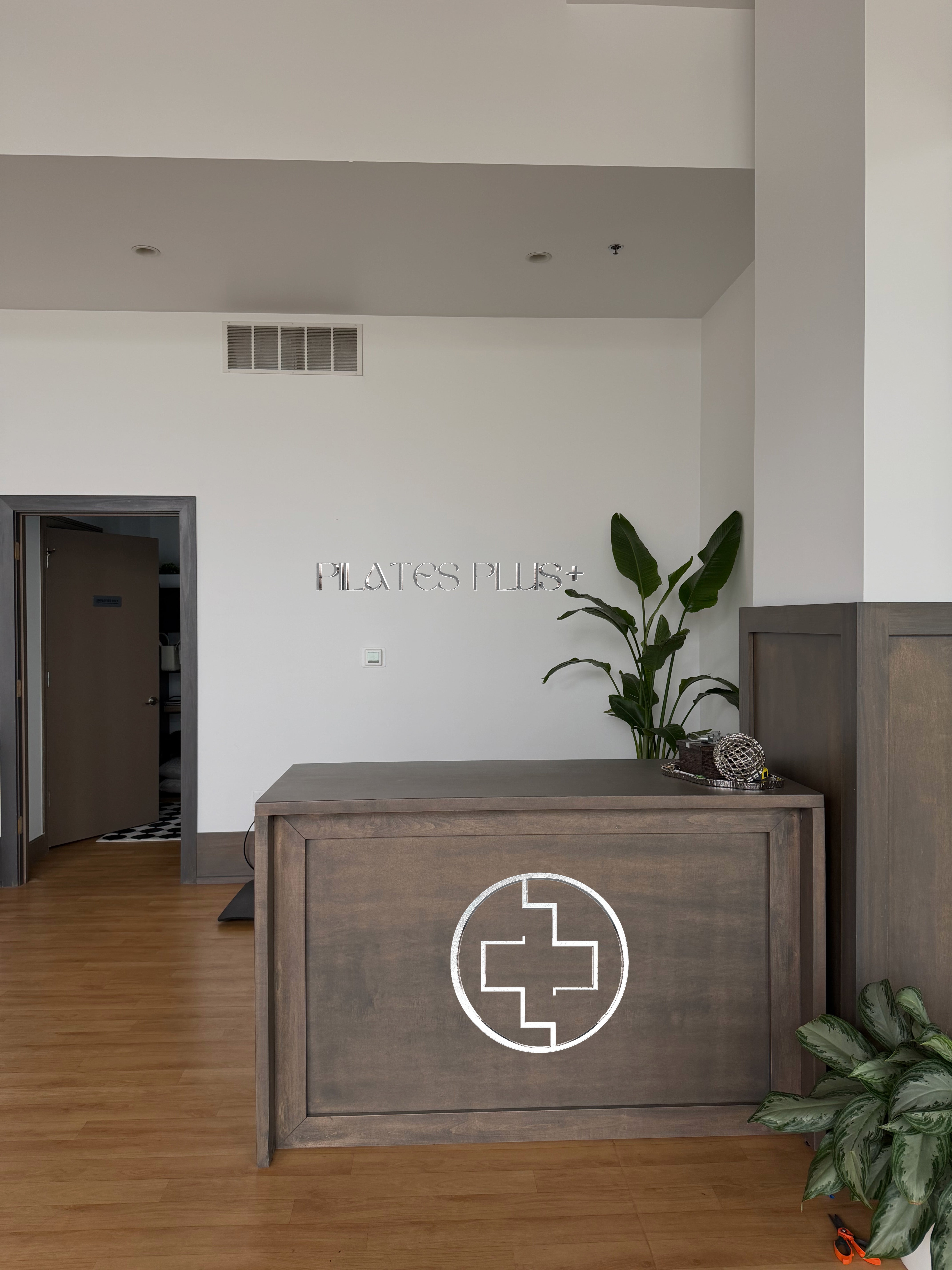 Custom Pilates Plus real installed reception sign by Volt Signs with chrome dimensional letters on wall and plus-cross emblem on wood reception desk.