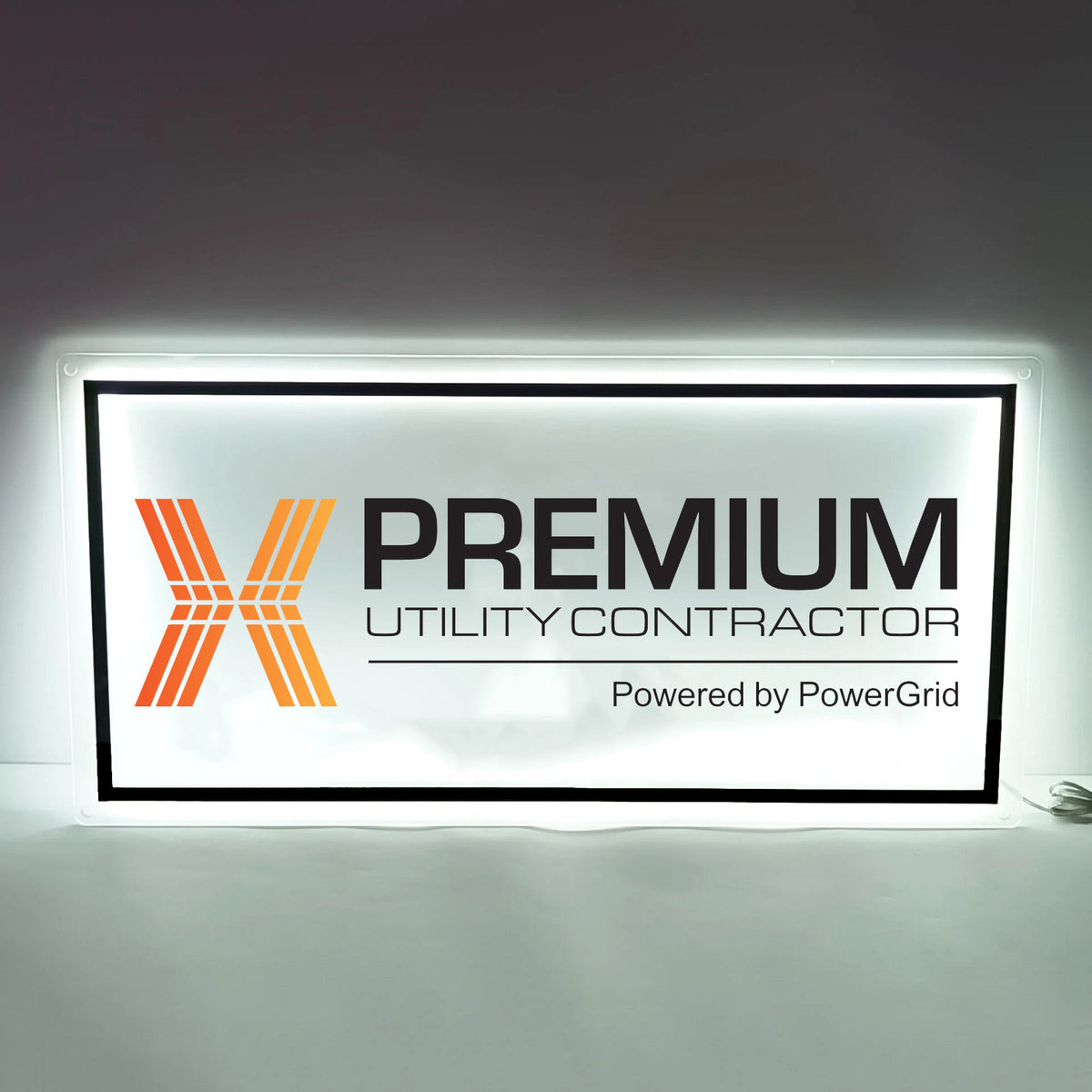 Backlit white rectangular sign with orange X logo, bold black PREMIUM text, 'UTILITY CONTRACTOR' and PowerGrid credit.