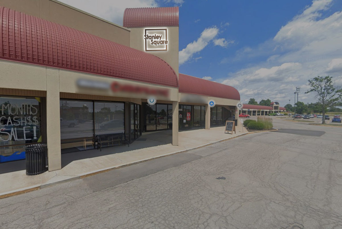 Stanley Square storefront with red curved awnings, beige facade, sidewalk bench, sandwich board and parking.