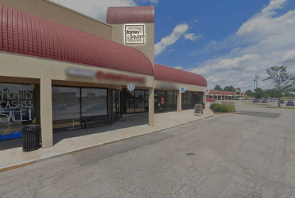 Stanley Square storefront with red curved awnings, beige facade, sidewalk bench, sandwich board and parking.