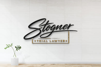 Black cursive 'Stogner' above gold-framed 'TRIAL LAWYER' on white tiled wall, glass vase with green leaves