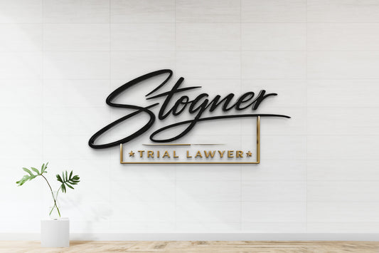 Black cursive 'Stogner' above gold-framed 'TRIAL LAWYER' on white tiled wall, glass vase with green leaves
