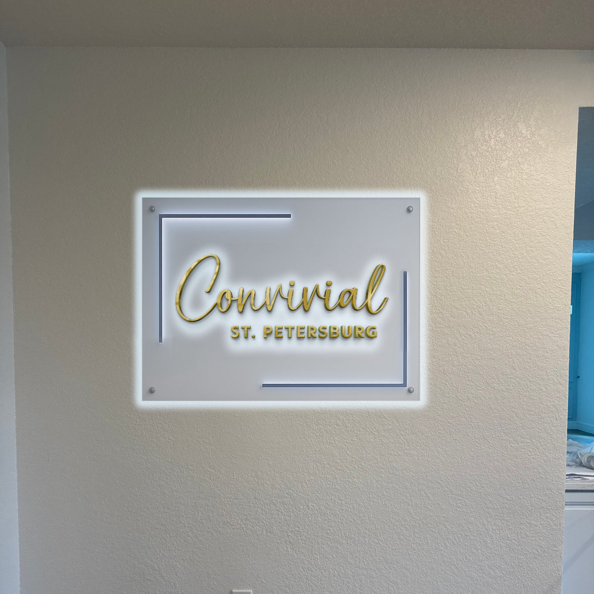 A backlit Convivial St. Petersburg acrylic sign is mounted on a textured wall as a Volt Signs custom signage display