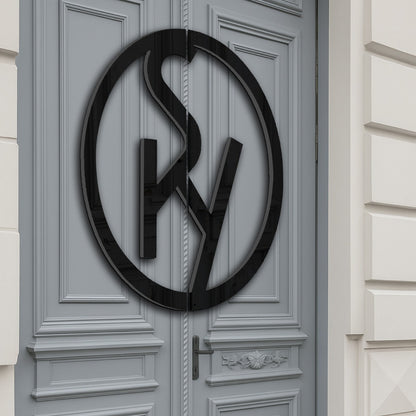 Gray ornate double doors with raised panel molding and a large glossy black circular monogram sign mounted at center.