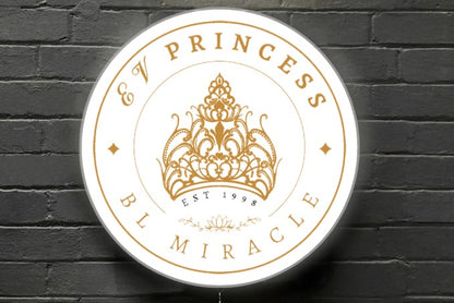 A round white sign with gold ornate crown, text 'PRINCESS', 'BL MIRACLE' and 'EST 1998' on a dark brick wall.