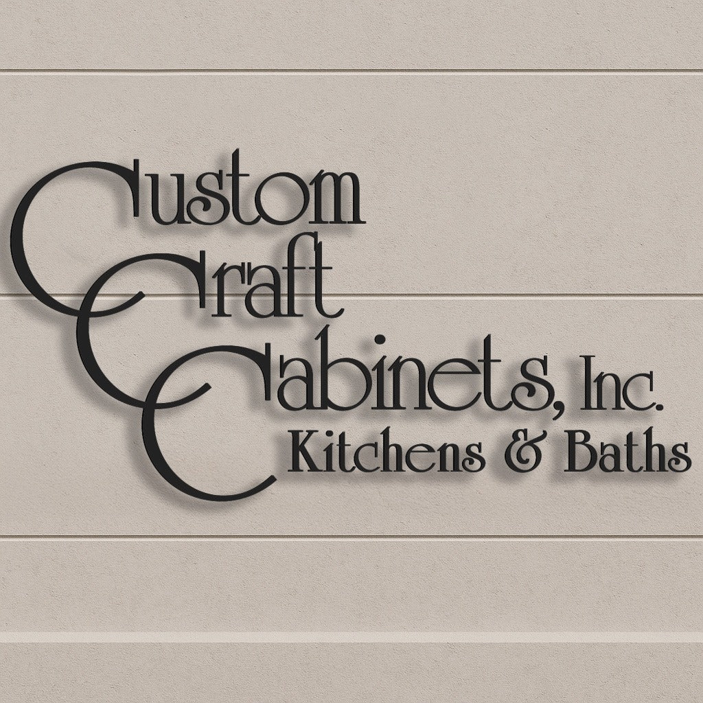 Black stylized lettering 'Custom Craft Cabinets, Inc. Kitchens & Baths' casts shadows on a beige textured wall.