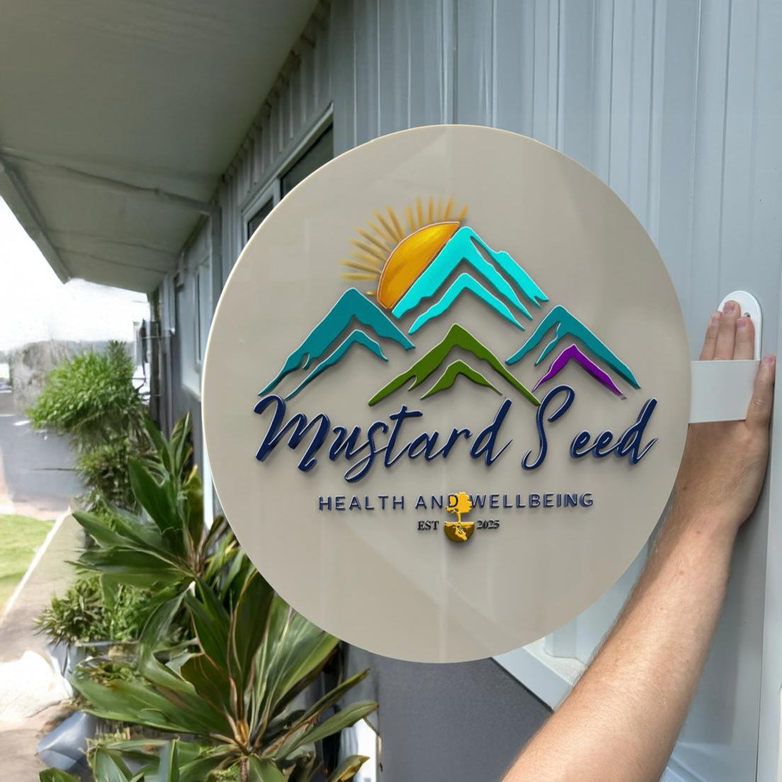 Round custom sign on a building reads Mustard Seed Health and Wellbeing with mountain logo, Volt Signs signage
