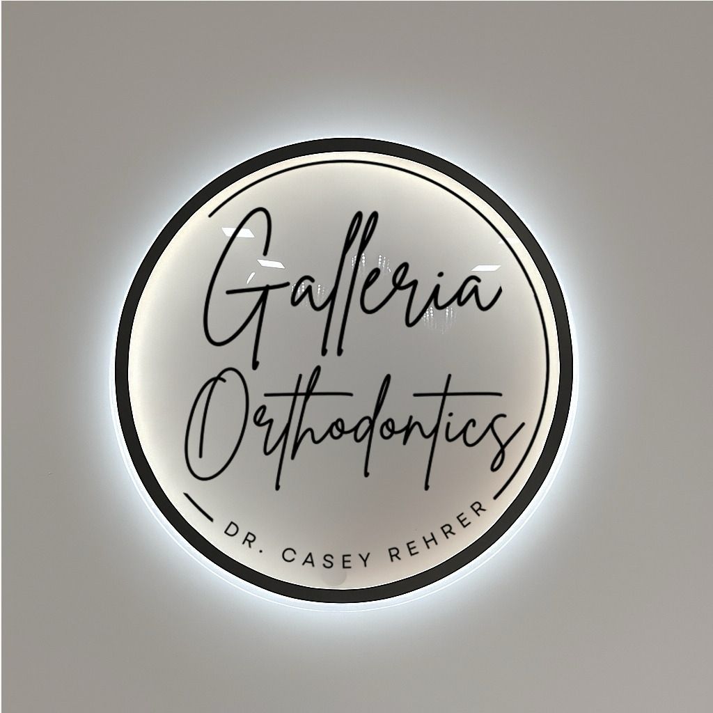 A round backlit sign with black script reading 'Galleria Orthodontics' and small text 'Dr. Casey Rehrer' on a gray wall.
