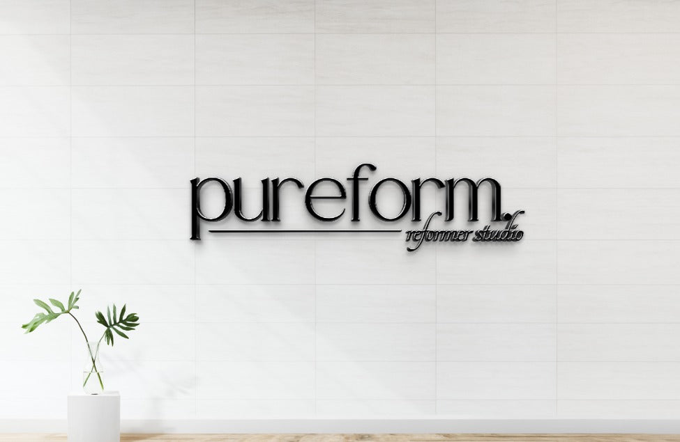 Black 3D 'pureform reformer studio' logo mounted on white tiled wall with underline, wooden floor, potted plant.