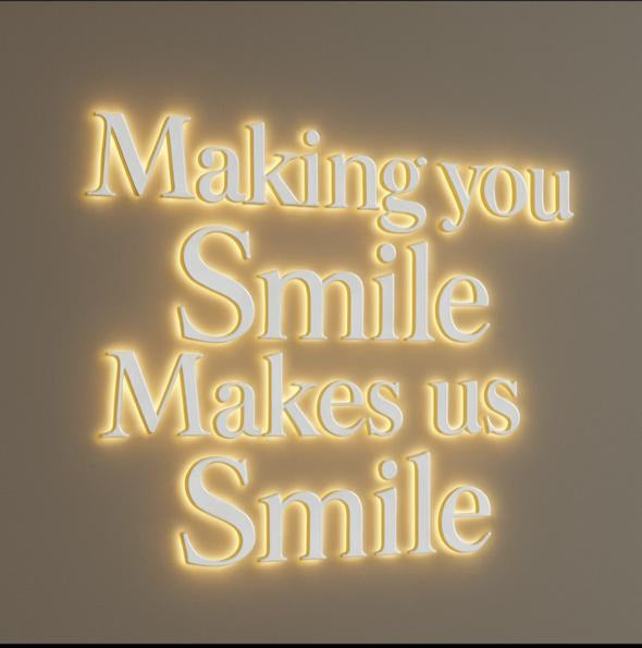 A Volt Signs illuminated custom sign and wall signage reads 'Making you Smile Makes us Smile' with warm halo lighting