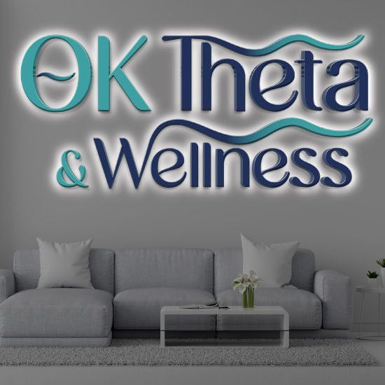 Volt Signs custom sign reading OK Theta & Wellness in teal and navy illuminated wall signage above a gray sofa