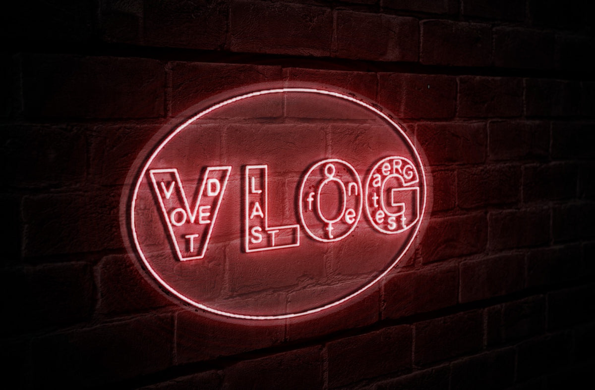 Red neon oval sign reading "VLOG" with tiny scattered letters inside each character, glowing on dark brick wall.
